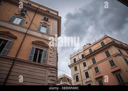 Vista verso l'alto di condomini ottocenteschi nel centro storico di Roma, con cornici ornate, persiane in legno e terrazze sul tetto che si affacciano su un cielo grigio mostruoso Foto Stock