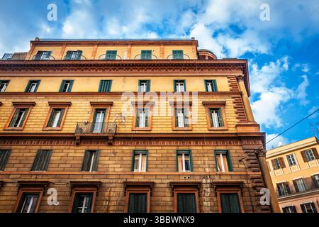 Vista verso l'alto di un palazzo residenziale di fine Ottocento nel centro storico di Roma, in italia, facciata in muratura ocra con persiane verdi che si illuminano in seguito Foto Stock
