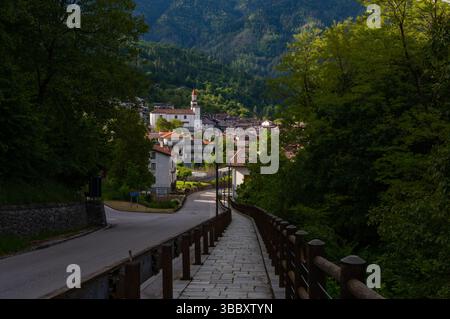 Una vista panoramica della piccola cittadina alpina di Sutrio, immersa in una valle lussureggiante, circondata da colline boscose e montagne Foto Stock