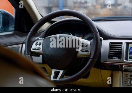 Interni della vettura. Interni lussuosi e moderni con volante in pelle nera, quadro strumenti digitale e interni in pelle beige. Foto Stock