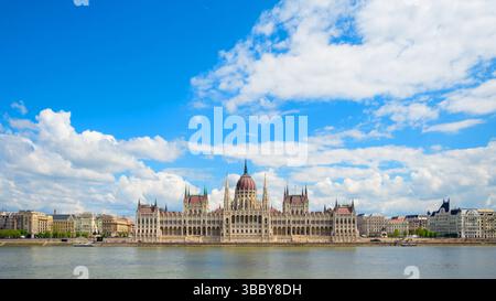 Gli edifici del Parlamento ungherese sorgono maestosamente lungo il Danubio a Budapest, sotto un cielo blu limpido pieno di nuvole. Mostra il Foto Stock