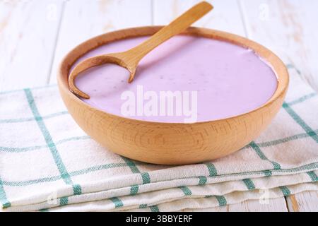 frullato di mirtilli in un recipiente di legno con cucchiaio su un tavolo bianco, messa a fuoco selettiva. Foto Stock