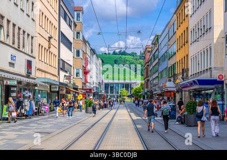 Wurzburg, Germania, 14 luglio 2024: Gente affollata che cammina lungo la strada pedonale con le rotaie del tram, turisti che passeggiano lungo la strada dello shopping con negozi e negozi Foto Stock
