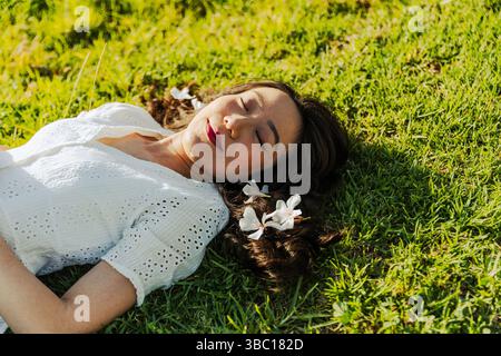 Una donna si sta sdraiando sull'erba con dei fiori nei capelli. Ha gli occhi chiusi. Foto Stock