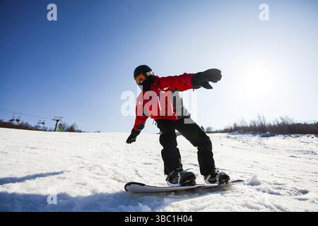 Ritratto vicino del giovane snowboarder freeriding la pista di neve in una giornata di sole inverno. Cielo blu su sfondo Foto Stock