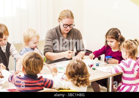 I bambini e i tutor sono la verniciatura con un pennello e acquerelli su carta nella scuola materna Foto Stock