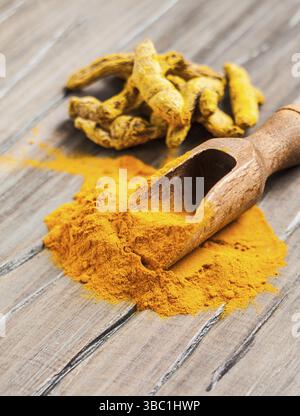 La curcuma spice - in polvere in un convogliatore e radici a secco su sfondo di legno Foto Stock