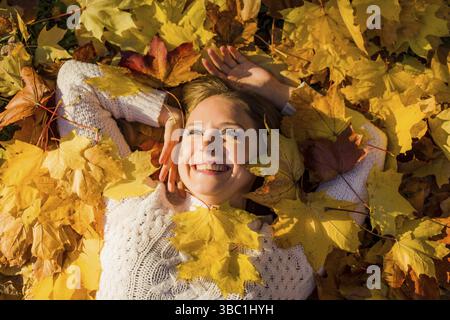 Donna che giaceva in foglie d'acero nel parco. Sole, caldo giorno e fogliame autunnale Foto Stock