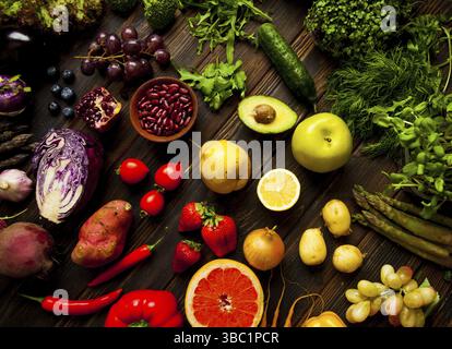 Set di verdure e frutta biologiche fresche multicolori adagiato su una superficie di legno scuro. Vasto assortimento di prodotti vegani Foto Stock