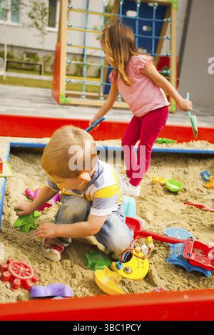 Bambini felici seduti in sandbox giocando con giocattoli colorati di plastica Foto Stock