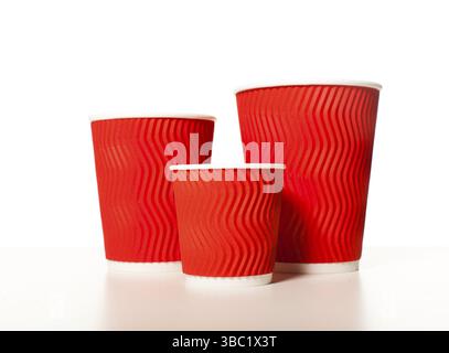 Tazze da caffè monouso in carta rossa di diverse dimensioni posizionate in fila su sfondo bianco, mockup per il design di espresso, cappuccino e latte Foto Stock