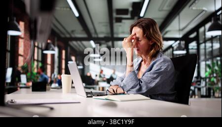 Il contabile stressato lavora con il tempo straordinario su un notebook con mal di testa e Ache Foto Stock