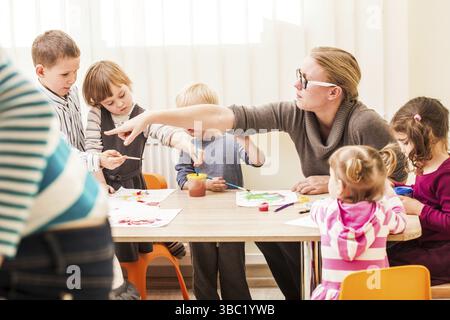 I bambini e i tutor sono la verniciatura con un pennello e acquerelli su carta nella scuola materna Foto Stock
