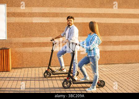 La giovane coppia di persone diverse sta viaggiando su scooter elettrici in giro per la città in estate Foto Stock