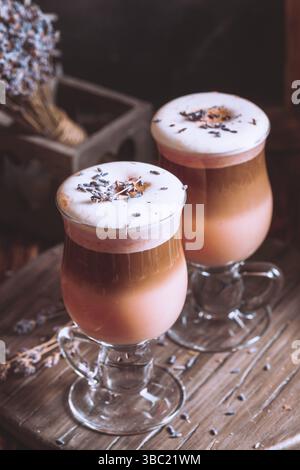 Foto primo piano di due grandi bicchieri di latte fragrante con grani di lavanda su un piedistallo di legno Foto Stock