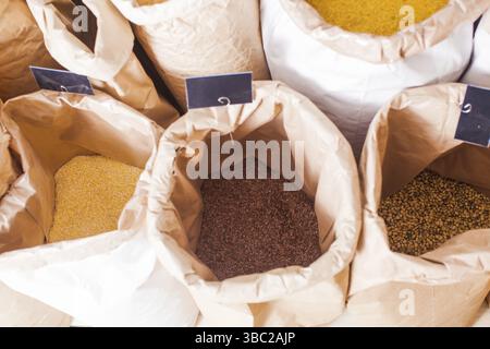 Grandi sacchetti di cartone con etichetta nera sui prezzi, pieni di raccolti e cereali, venduti al supermercato. I cereali venduti in pesatura presso il negozio di rifiuti zero Foto Stock