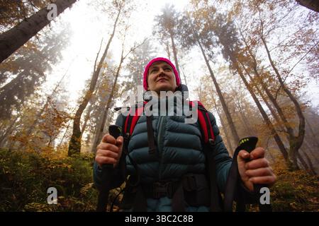 Donna attiva escursioni in bella foresta autunnale. Ritratto di felice giovane donna sorridente con attrezzatura da nordic walking Foto Stock