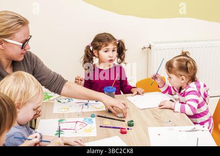 I bambini e i tutor sono la verniciatura con un pennello e acquerelli su carta nella scuola materna Foto Stock