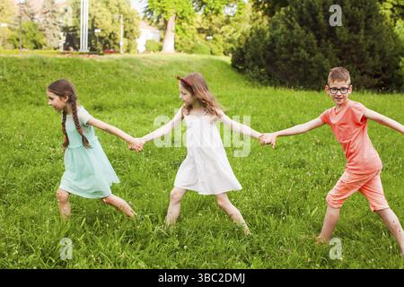 I bambini seguono in linea le mani di golding. Gruppo di bambini giocano sull'erba verde tenendo le mani Foto Stock