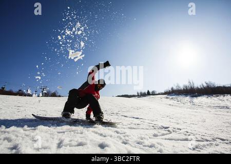 Snowboarder maschio nel momento di cadere sulla neve. Nuvola di neve sulla testa. Cielo blu con sole luminoso su uno sfondo Foto Stock