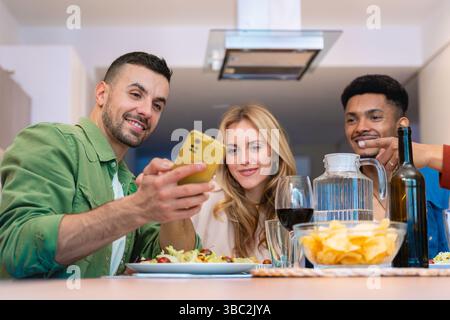 Amici multietnici felici gustando spuntini e bevande in una cucina moderna e luminosa Foto Stock