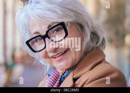 Felice donna caucasica senior con cappotto e bicchieri in piedi nell'area caffetteria all'aperto Foto Stock