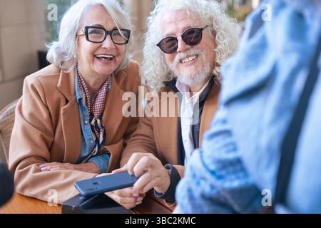 Coppia senior felice con smartphone sorridente e divertendosi all'aperto Foto Stock