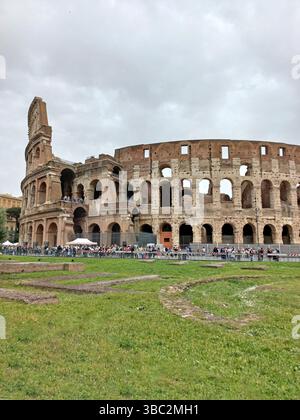 Roma, Lazio, Italia. 15 aprile 2025. Le persone che visitano il Colosseo Romano, in piedi sulla piazza acciottolata mentre ammirano l'iconico anfiteatro Foto Stock
