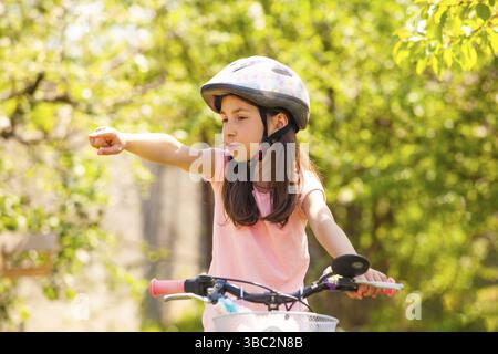 Ragazza che corre in bicicletta all'aperto e mostra il sentiero a mano Foto Stock