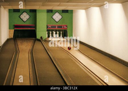 Scena di bowling che mostra una palla rossa che rotola verso i birilli in una corsia vuota. L'immagine cattura il momento di attesa in una classica pista da bowling con Foto Stock