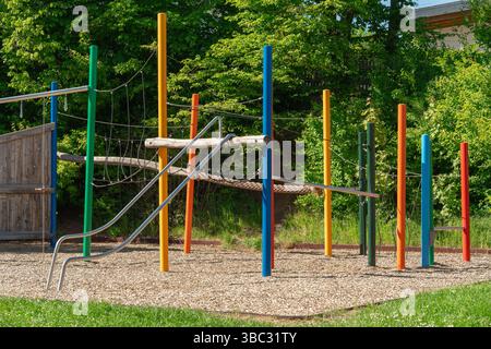Parco giochi dai colori vivaci con scivolo, funi da arrampicata e pali verticali in un parco soleggiato. Circondato da una vegetazione lussureggiante, crea un Foto Stock