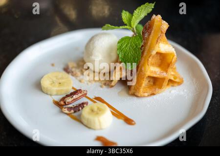 Waffle con gelato alla vaniglia servito con noci, banana e salsa al caramello Foto Stock