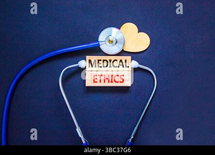 Simbolo di etica medica. Parole concettuali etica medica su bellissimi blocchi di legno. Cuore in legno e stetoscopio. Splendido sfondo nero. Guarigione medica Foto Stock