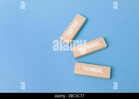 Tre blocchi di legno con le parole "contenuto", "parole chiave" "tecnico" su sfondo blu, che simboleggiano il concetto SEO Foto Stock