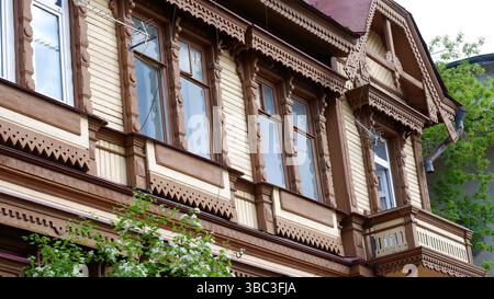 Edificio in legno marrone vintage in una città moderna. Tradizionale architettura russa, finestre in legno con cornici intagliate. Motivo decorativo intagliato del Foto Stock