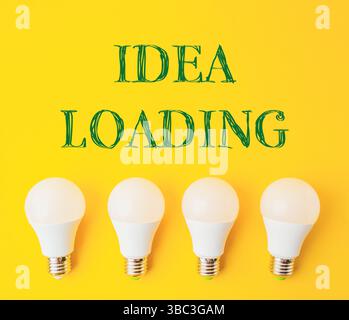 Quattro lampadine bianche su sfondo giallo con la parola idea Loading scritta in verde. Foto Stock
