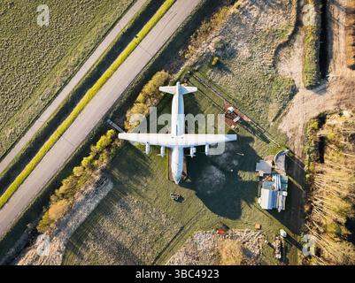 Vecchio aereo ad elica dimenticato nel tempo: Vista aerea di un aereo solitario che si ripone in un campo da una strada al tramonto. Foto Stock