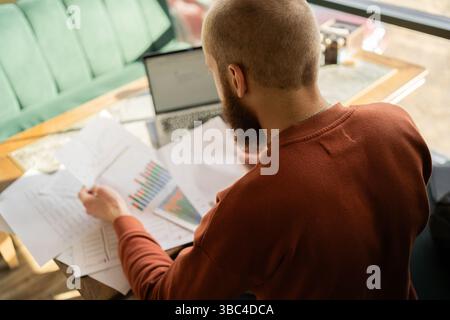 Uomo d'affari che utilizza un computer portatile e si occupa di grafici e grafici seduti al tavolo dell'ufficio Foto Stock