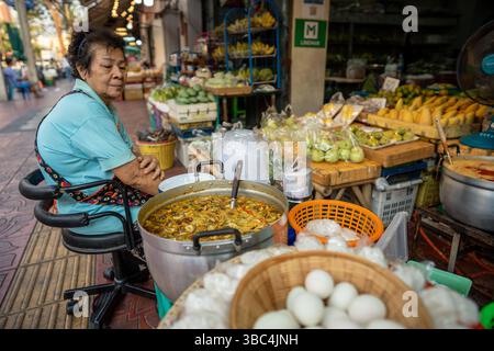 La donna calma aspetta gli acquirenti al chiosco di cibo di strada che serve zuppa di curry fumante da pentola grande Foto Stock
