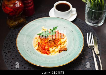 Piatto di tagliatelle condito con abbondante salsa di pomodoro, guarnito con prezzemolo, servito con una tazza di caffè nero. Foto Stock