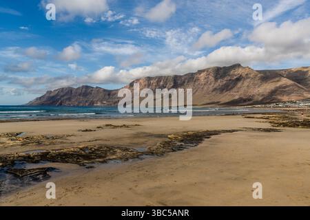 Le scogliere di Famara si innalzano fino a 671 metri sopra la spiaggia deserta di Playa de Famara a Lanzarote. Sono i resti di una caldera larga circa dieci chilometri centrata a sud dell'isola vicina di La Graciosa. Caleta de Famara, Isole Canarie, Spagna. Foto Stock