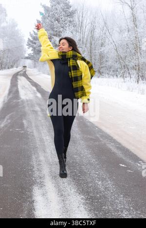 Una ragazza con un cappotto giallo cammina lungo una strada invernale Foto Stock