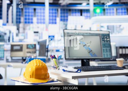 Programma CAD su display PC in impianti fotovoltaici utilizzati per la progettazione di linee di produzione. Software di simulazione su monitor del computer in un impianto di pannelli solari vuoto accanto al cappello giallo Foto Stock