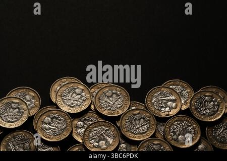 Monete britanniche sparse da una sterlina lungo il bordo inferiore di uno sfondo nero, che rappresentano risparmi, guadagni e valuta del Regno Unito, Stafford, Regno Unito Foto Stock