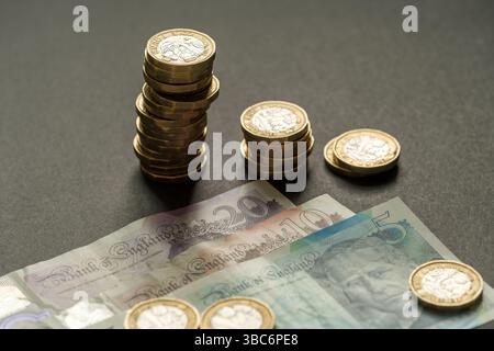 Pile di monete inglesi da una sterlina disposte in altezza decente accanto a banconote da 5, 10 e 20, simboleggiando lo stato finanziario e il risparmio, Stafford, United Foto Stock