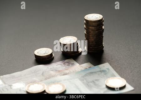 Le monete da una sterlina britannica in ordine ascendente collocate sopra le banconote da 5, 10 e 20, rappresentando la crescita finanziaria e il risparmio, Stafford, Unite Foto Stock