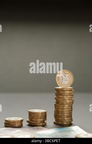 Immagine verticale di monete da una sterlina impilate che formano un grafico a barre in aumento con le banconote britanniche in primo piano, simboleggiando la crescita del reddito e la suc finanziaria Foto Stock