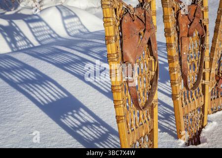 Dettaglio delle racchette da neve vintage Bear Paw in legno con rilegatura in pelle nella neve con ombra Foto Stock