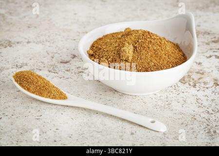 Piccola ciotola in ceramica con zucchero di palma da cocco non raffinato su uno sfondo piastrellato in ceramica con un cucchiaio Foto Stock
