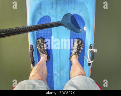 Narrow racing stand up paddleboard with a carbon fiber paddle and paddler feet in water sandals - top view Stock Photo